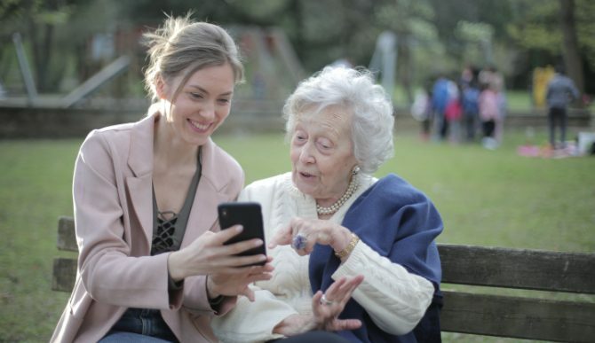 Mladá žena a stará žena při pohledu na telefon na lavičce