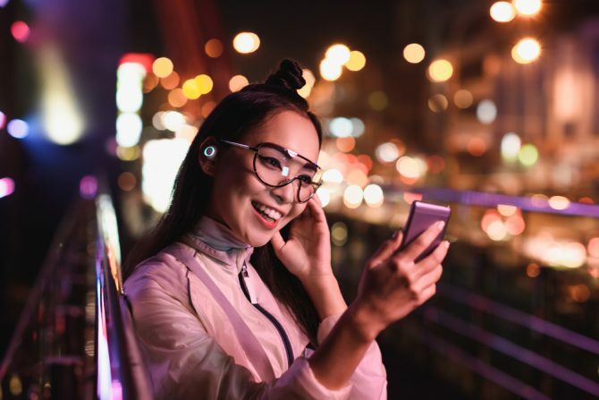 šťastná Asijská dívka s video chat pomocí smartphone a do uší sluchátka